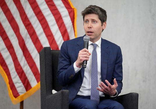 Sam Altman, CEO of OpenAI, sitting in front of American flag